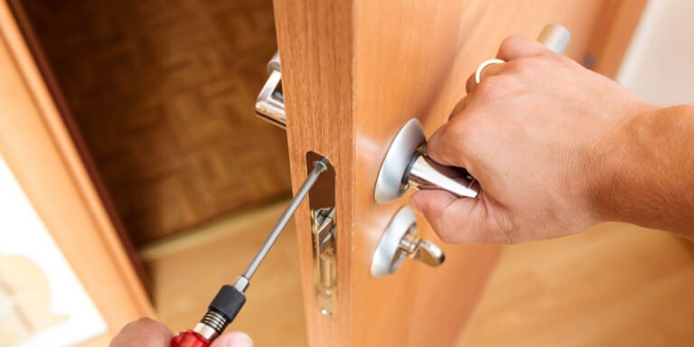 Un serrurier répare une serrure multipoints sur une porte en bois avec un tournevis.