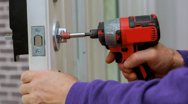 Un serrurier utilise une visseuse pour remplacer une serrure de porte métallique.